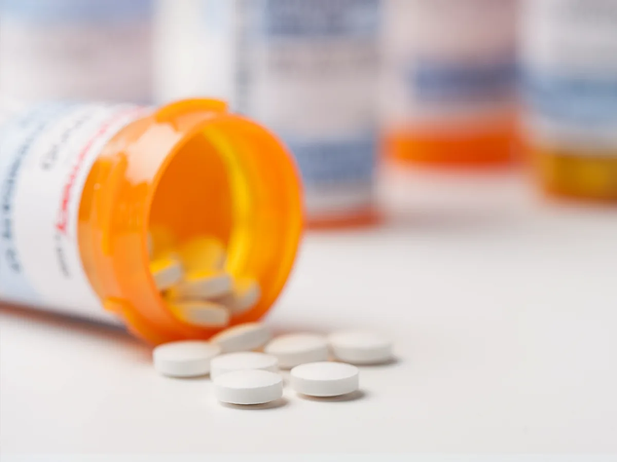 A pill container on its side spilling pills out. Pill containers in the distance.